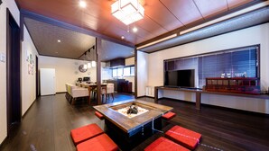 A modern living room with a wooden coffee table, red cushioned seating, a kitchen area with a TV, and a dining space with chairs. - ID STAY Kawaguchiko 3 (Fujikawaguchiko)