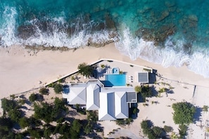Vista aérea de una propiedad frente a la playa con piscina, varios edificios y una playa de arena.