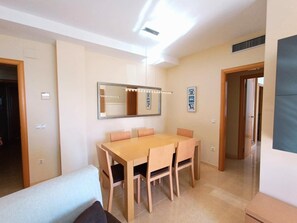 A dining area with a wooden table and chairs, a large mirror with lights, and a door leading to another room.