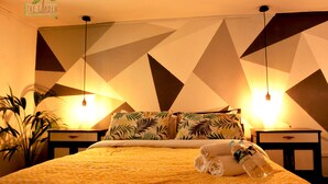 A hotel room with a geometric patterned wall, a bed with a yellow patterned bedspread, two bedside tables with lamps, and a potted plant. - The Garden Bed and Breakfast (Las Palmas de Gran Canaria)
