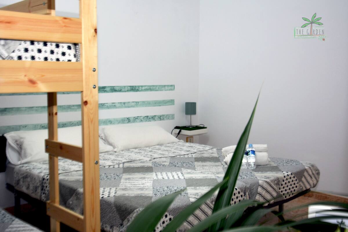 A bedroom with a bunk bed, a bedside table with a lamp, and a bed with a patterned blanket.
