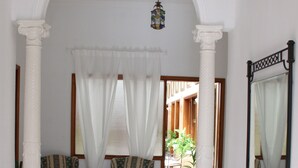 A hallway with a white floor, two upholstered chairs, a glass console table, and a mirror on the wall. - The Garden Bed and Breakfast (Las Palmas de Gran Canaria)