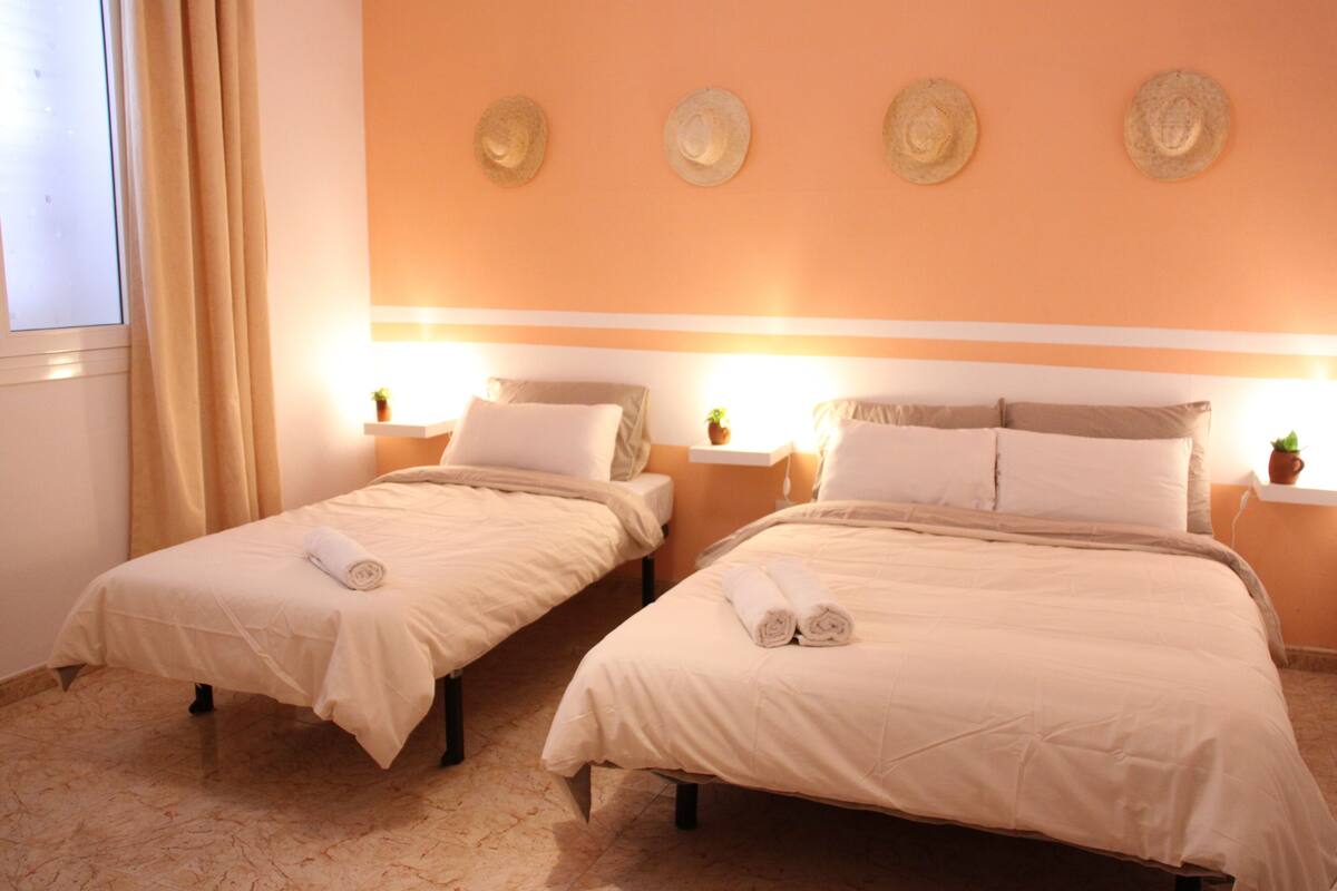 A hotel room with two beds, beige bedding, and a wall with four hats.
