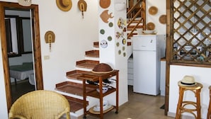 Une cuisine équipée d’un réfrigérateur, d’un tabouret en bois et d’une chaise en osier.