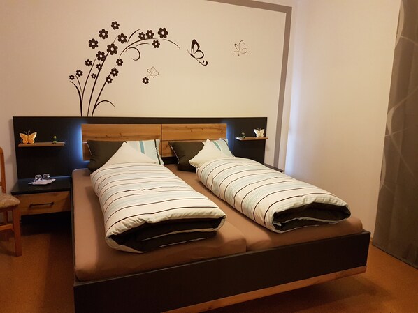 A double bed with striped bedding, a wooden headboard, bedside tables with decorative butterflies, and wall art featuring flowers and butterflies.