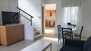 Ein modernes Wohnzimmer mit Flachbildfernseher, einer Couch, einem Couchtisch und einer Essecke mit Stühlen und Tisch.