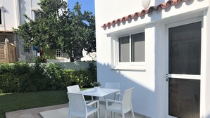 Eine Terrasse mit Tisch und Stühlen, eine Glastür und eine weiße Außenwand.