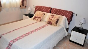 A neatly made bed with patterned pillows, a bedside table with a lamp, and a wall-mounted decorative item. - Apartment Barcino - Calafell (CALAFELL)