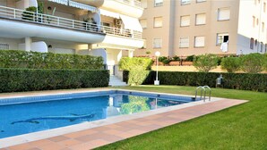 A swimming pool with a tiled deck, surrounded by well-maintained grass and hedges. - Apartment Barcino - Calafell (CALAFELL)