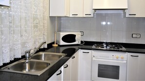 A kitchen with white cabinets, a stainless steel sink, a microwave, and a stove. - Apartment Barcino - Calafell (CALAFELL)