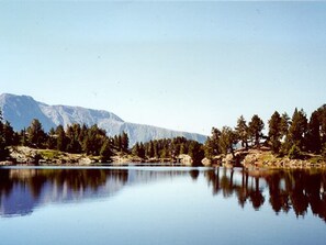 Un lac paisible, avec des montagnes en arrière-plan et des arbres le long de la rive.