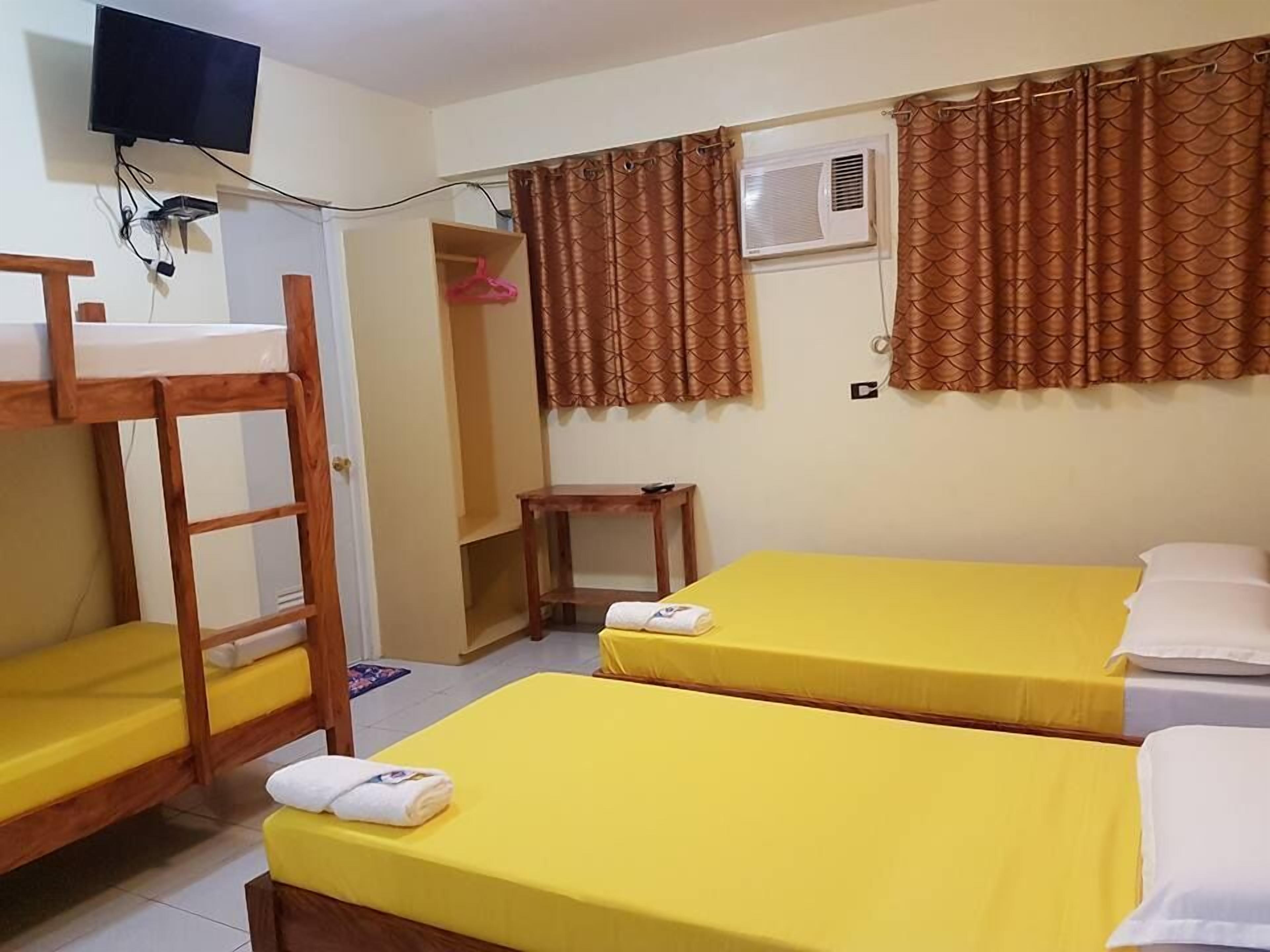 A room with bunk beds, a desk, a chair, a TV, and an air conditioning unit.