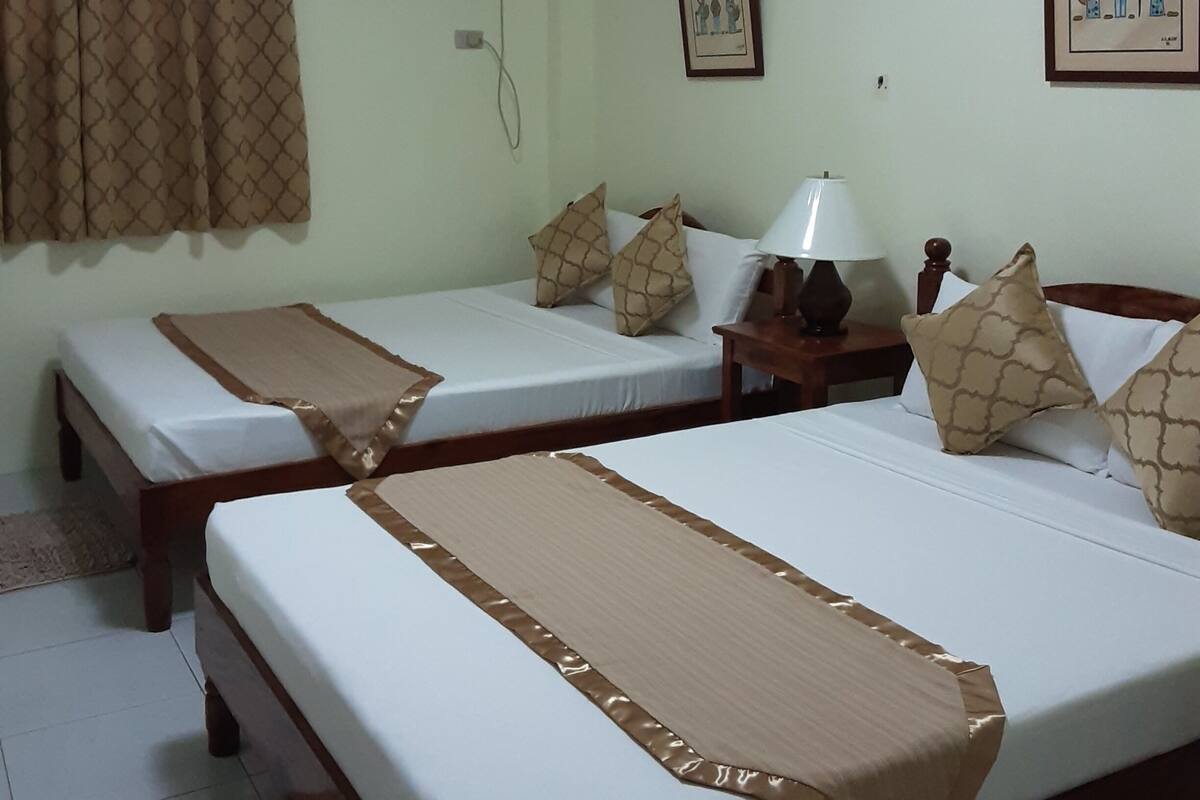 A hotel room with two single beds, a bedside table with a lamp, a wall-mounted air conditioner, and a framed picture.