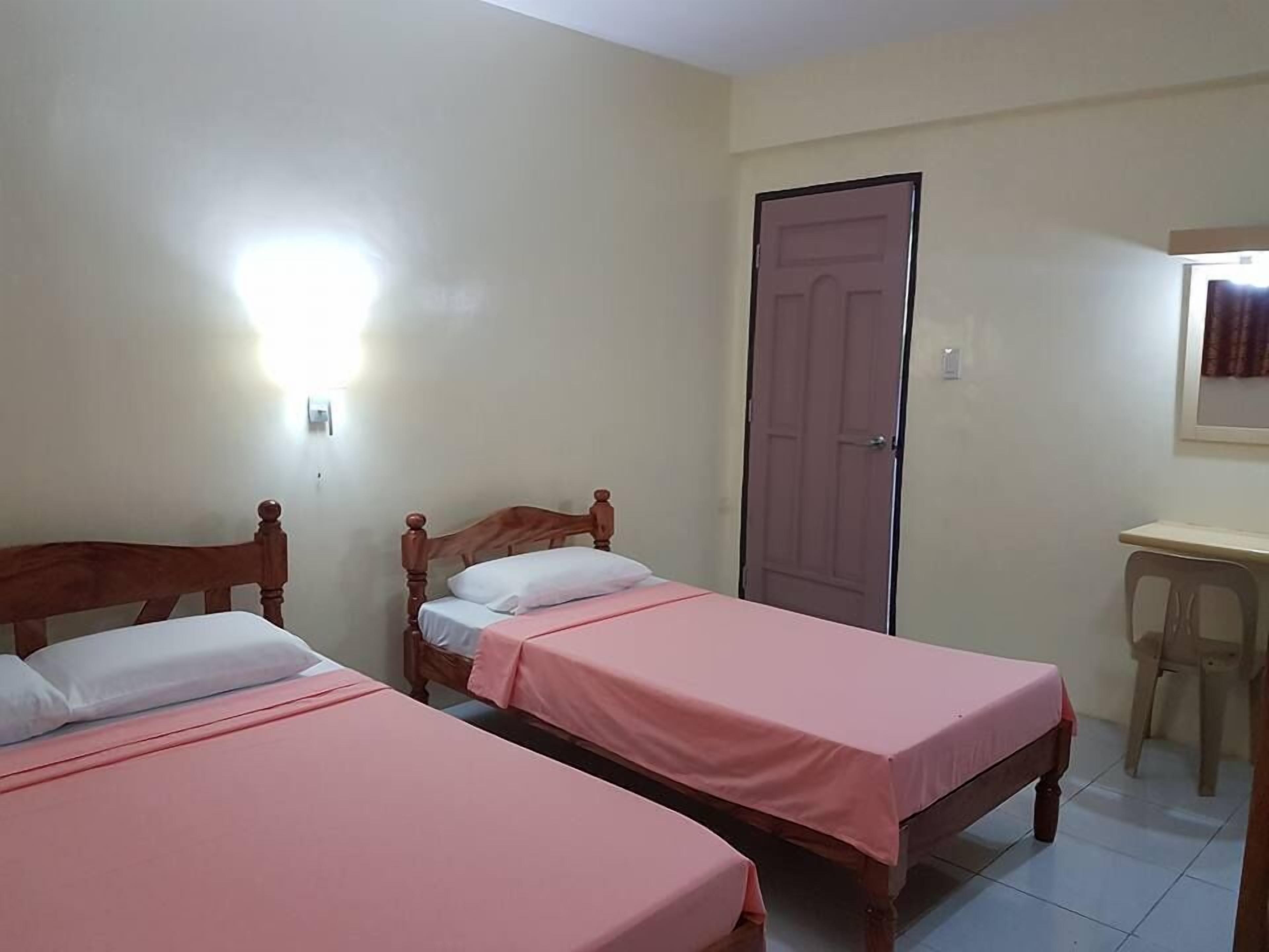 Une pièce avec deux lits en bois, dotés de draps roses, un bureau en bois et une porte.