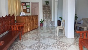 A reception area with a wooden desk, a reception counter, a staircase, and a seating area with chairs. - Batanes Casa Feliciano (Basco)