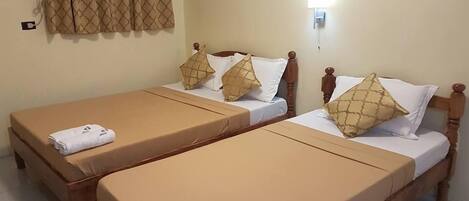 A hotel room with two single beds, each with a wooden headboard, beige bedsheets, and matching pillows. There is a wall-mounted light fixture above the beds.