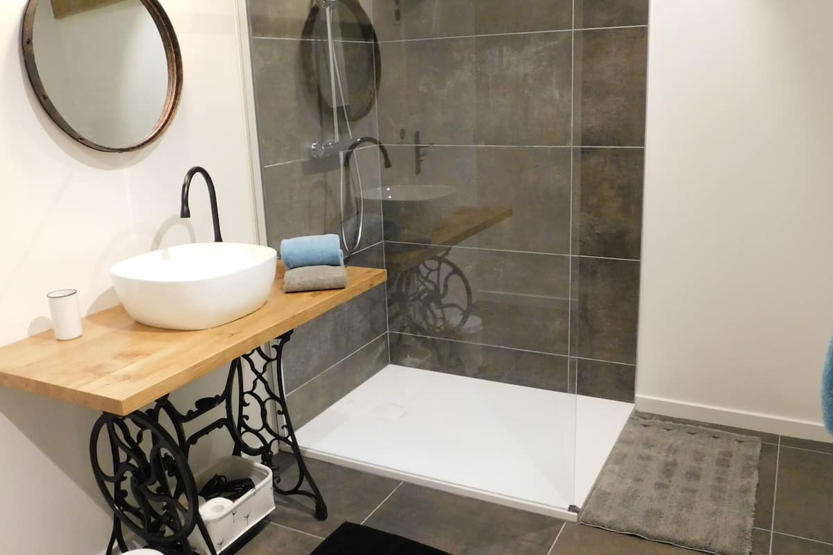 A bathroom with a wooden vanity, a round mirror, a white sink, and a shower with a glass door.