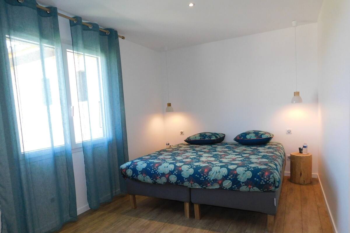 A bedroom with a bed, curtains, bedside lamps, and a small wooden stool.