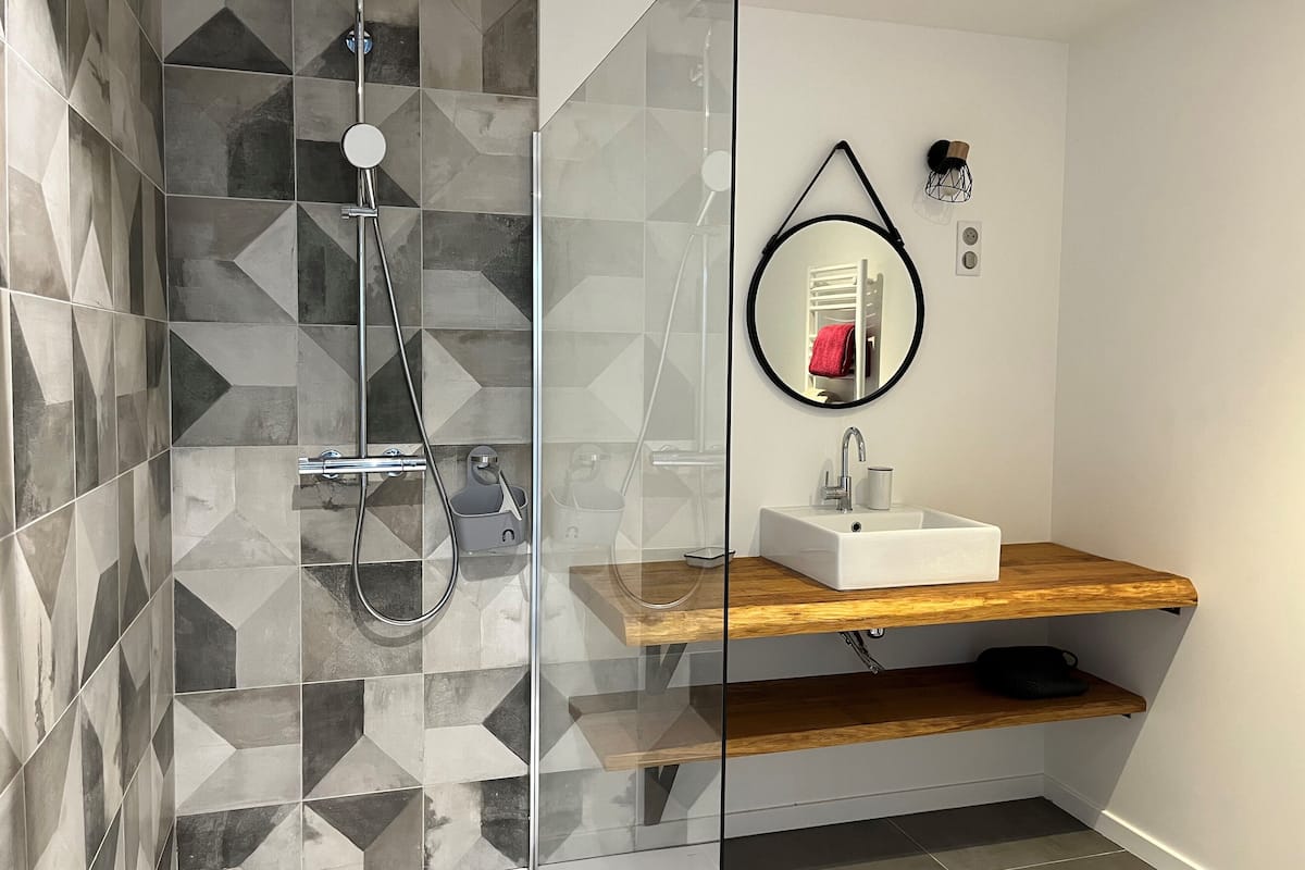 A modern bathroom with a glass shower enclosure, a white sink, and a wooden shelf.