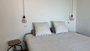 A bedroom with a bed, two patterned pillows, a wooden stool, and two hanging light fixtures. - La Maison de Paul & Margaux (Chateauneuf-de-Galaure)
