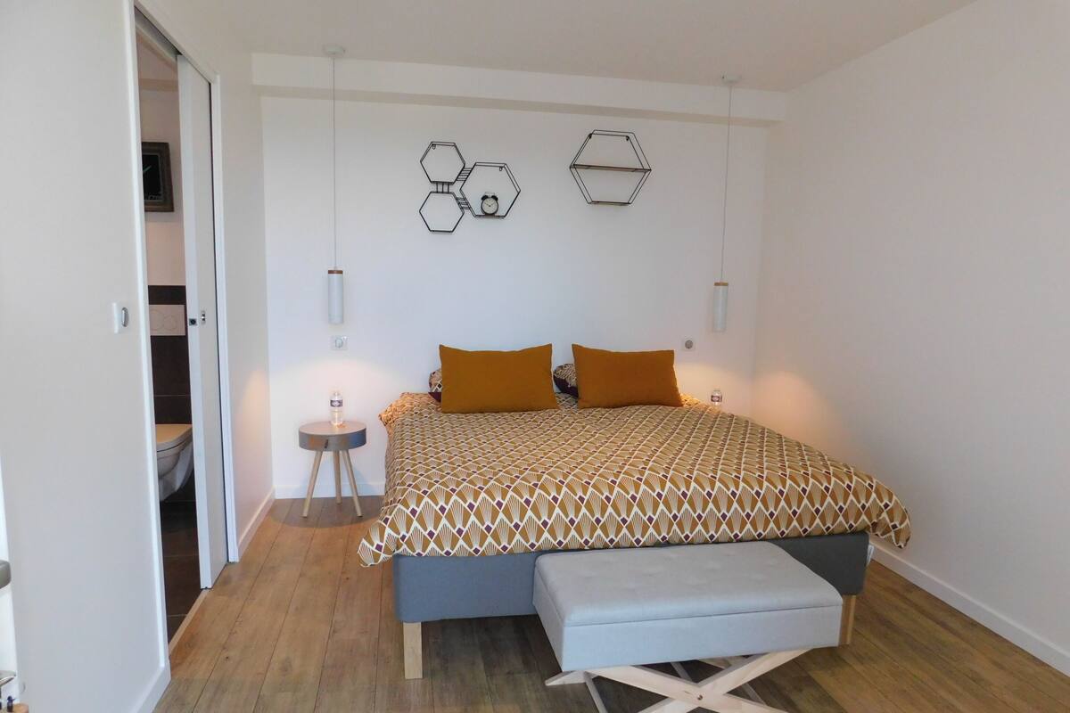 A bedroom with a bed, a bench, a small table, and a wall with hexagonal decorations.