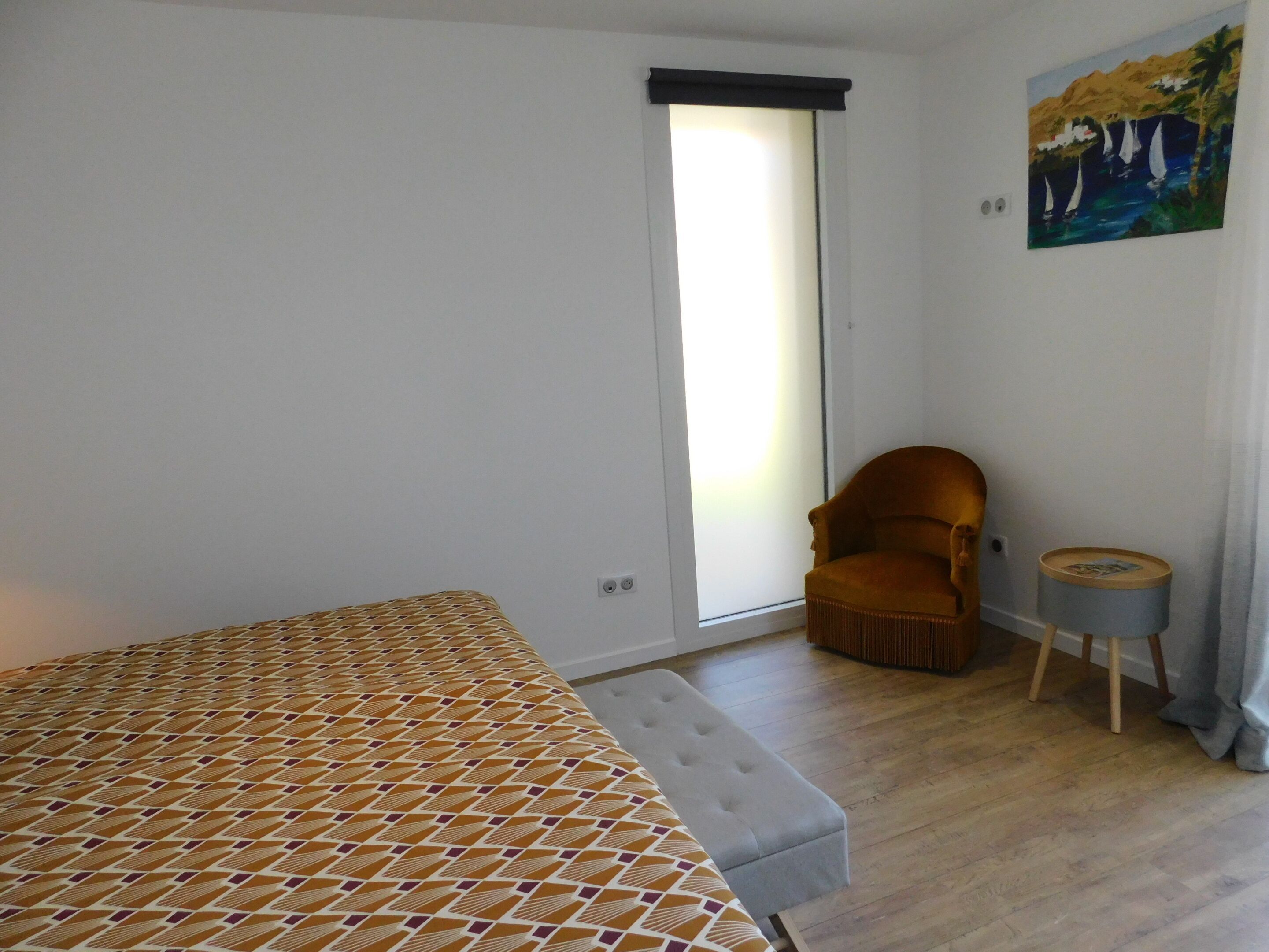 Una camera da letto con un letto, una sedia, un tavolino e un quadro appeso al muro.