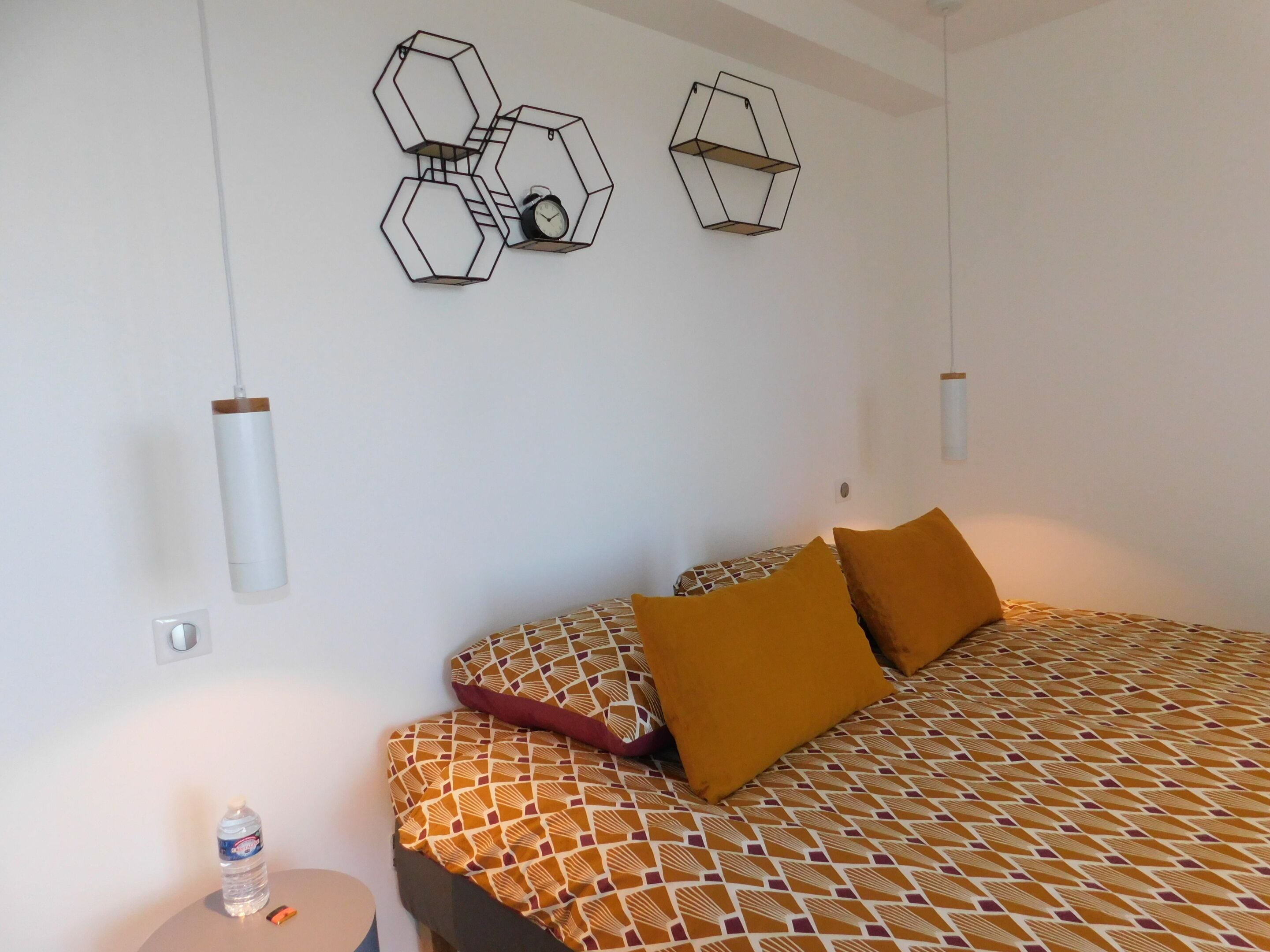 A bedroom with a patterned bedspread, two pillows, a water bottle, and a clock on the wall.