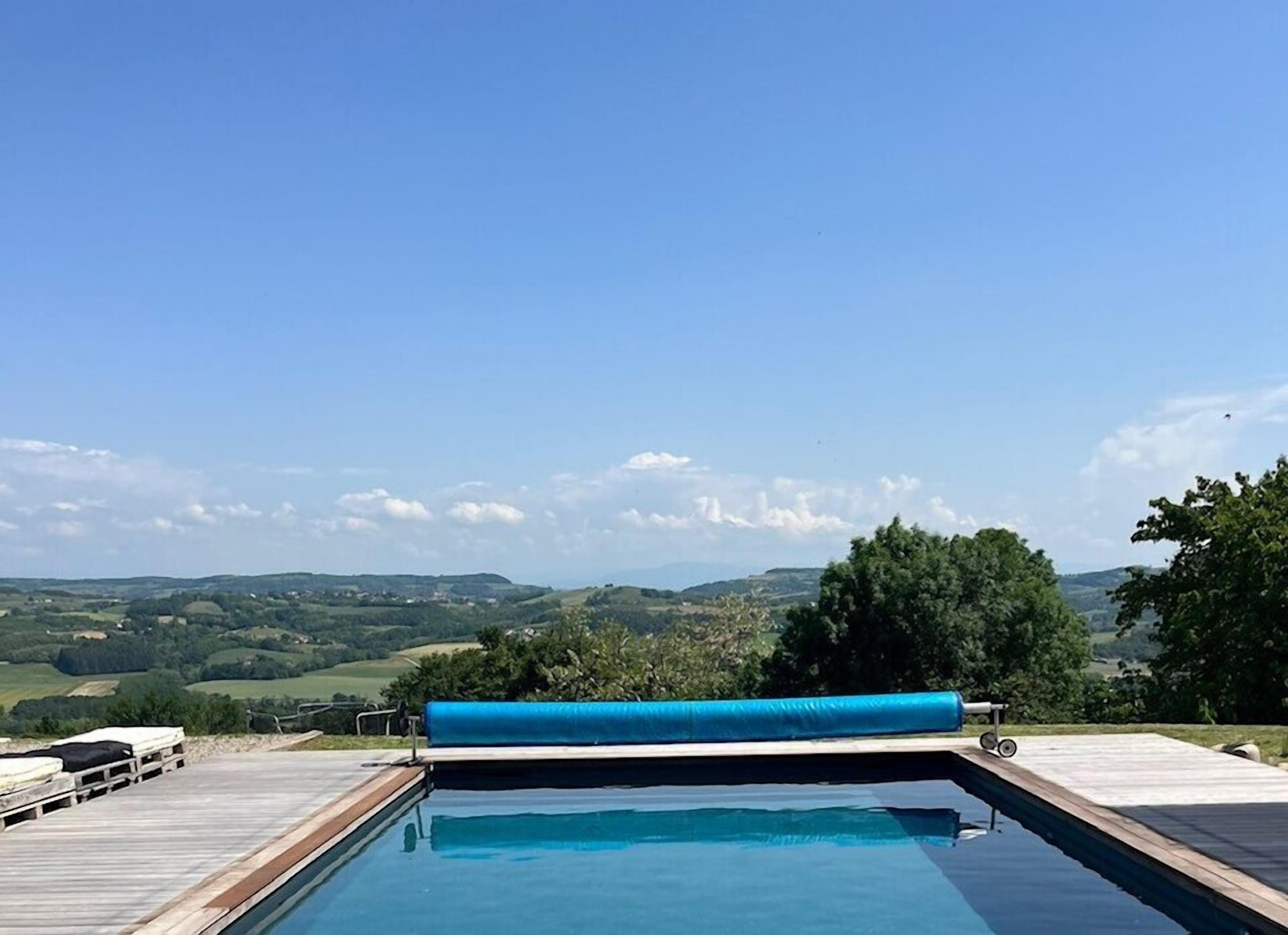 Una piscina con cubierta de madera y colchoneta azul, rodeada de un paisaje pintoresco.