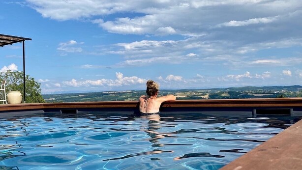 A person relaxing in a clear pool with a view of distant hills and a partly cloudy sky. - La Maison de Paul & Margaux (Chateauneuf-de-Galaure)