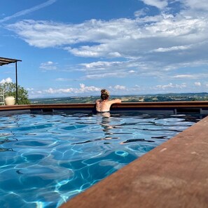Una persona relajándose en una piscina cristalina con vistas a colinas distantes y un cielo parcialmente nublado.