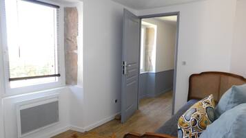 A room with a large window, a radiator, a wicker chair, and a patterned throw pillow.