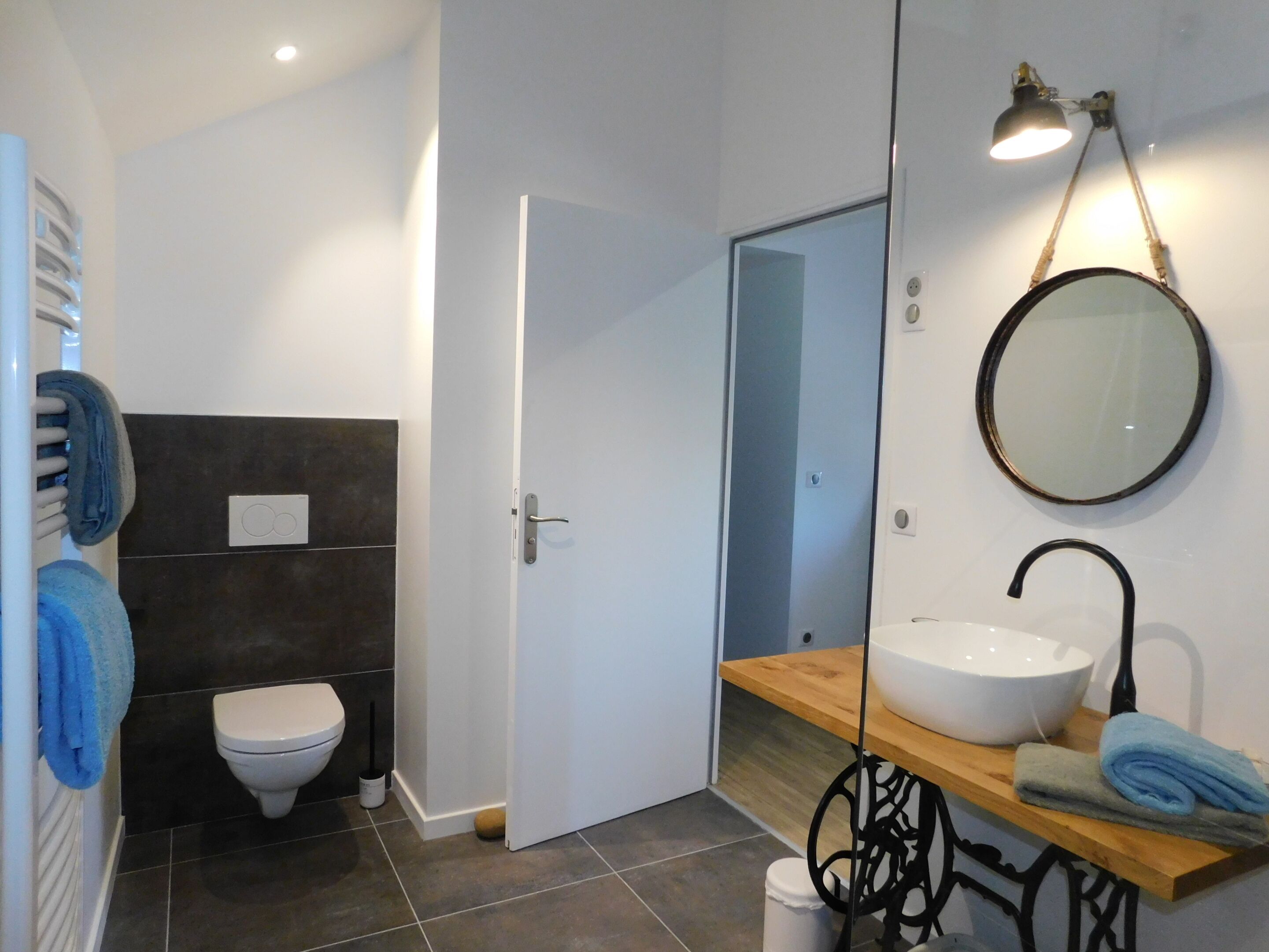 A bathroom with a white toilet, a sink with a wooden countertop, a mirror, and a towel rack with blue towels.