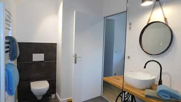 A bathroom with a white toilet, a sink with a wooden countertop, a mirror, and a towel rack with blue towels.