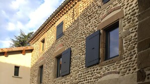 A stone building with multiple windows and doors, a grassy area in front, and a clear sky. - La Maison de Paul & Margaux (Chateauneuf-de-Galaure)