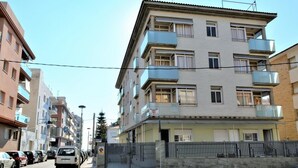 Un edificio residencial de varios pisos con balcones, un acceso con portón y automóviles estacionados a lo largo de la calle.