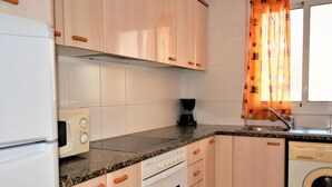 Cocina compacta con armarios de madera, horno empotrado, microondas y lavadora.
