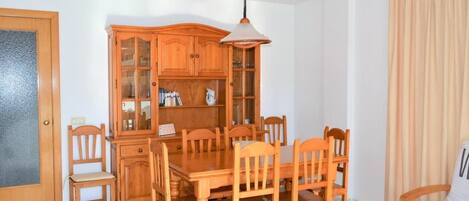 A dining area with a wooden table and chairs, a cabinet with glass doors, and a hanging light fixture.