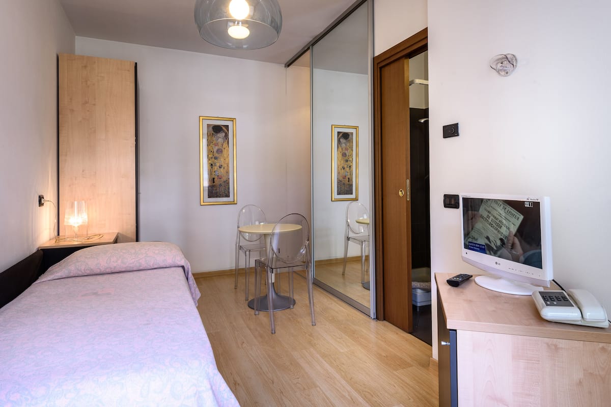 Ein Hotelzimmer mit einem Bett, einem Schreibtisch mit Computer, einem Sessel und einem Fernseher.