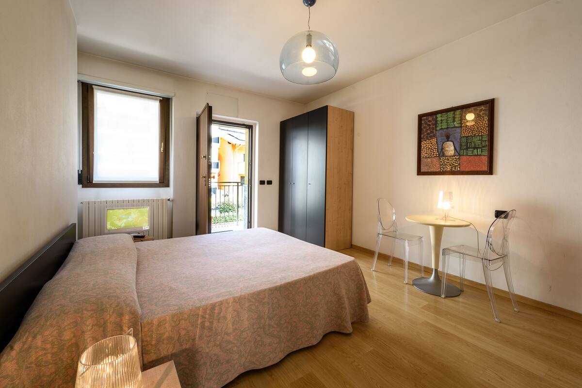 Ein Schlafzimmer mit Bett, Schreibtisch und Stuhl. Ein Fenster und eine Tür führen zu einem Balkon.