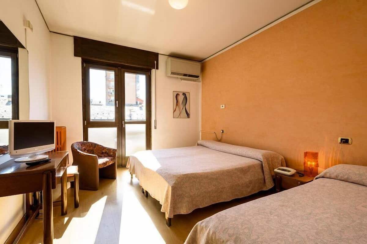 Ein Hotelzimmer mit zwei Betten, einem Schreibtisch mit Computer, einem Stuhl und einem Fenster mit Blick.