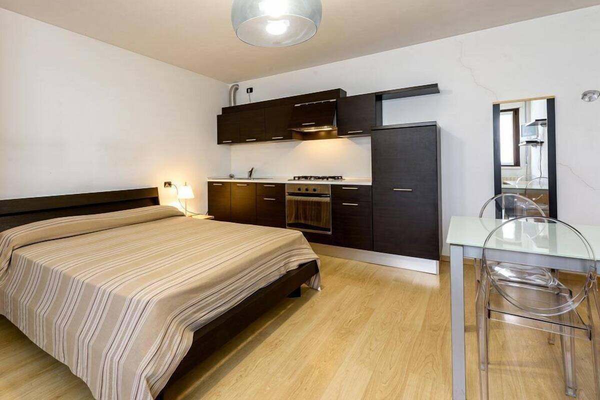 Ein Schlafzimmer mit Bett, Schreibtisch, Stuhl, Kleiderschrank und einer Küchenzeile.