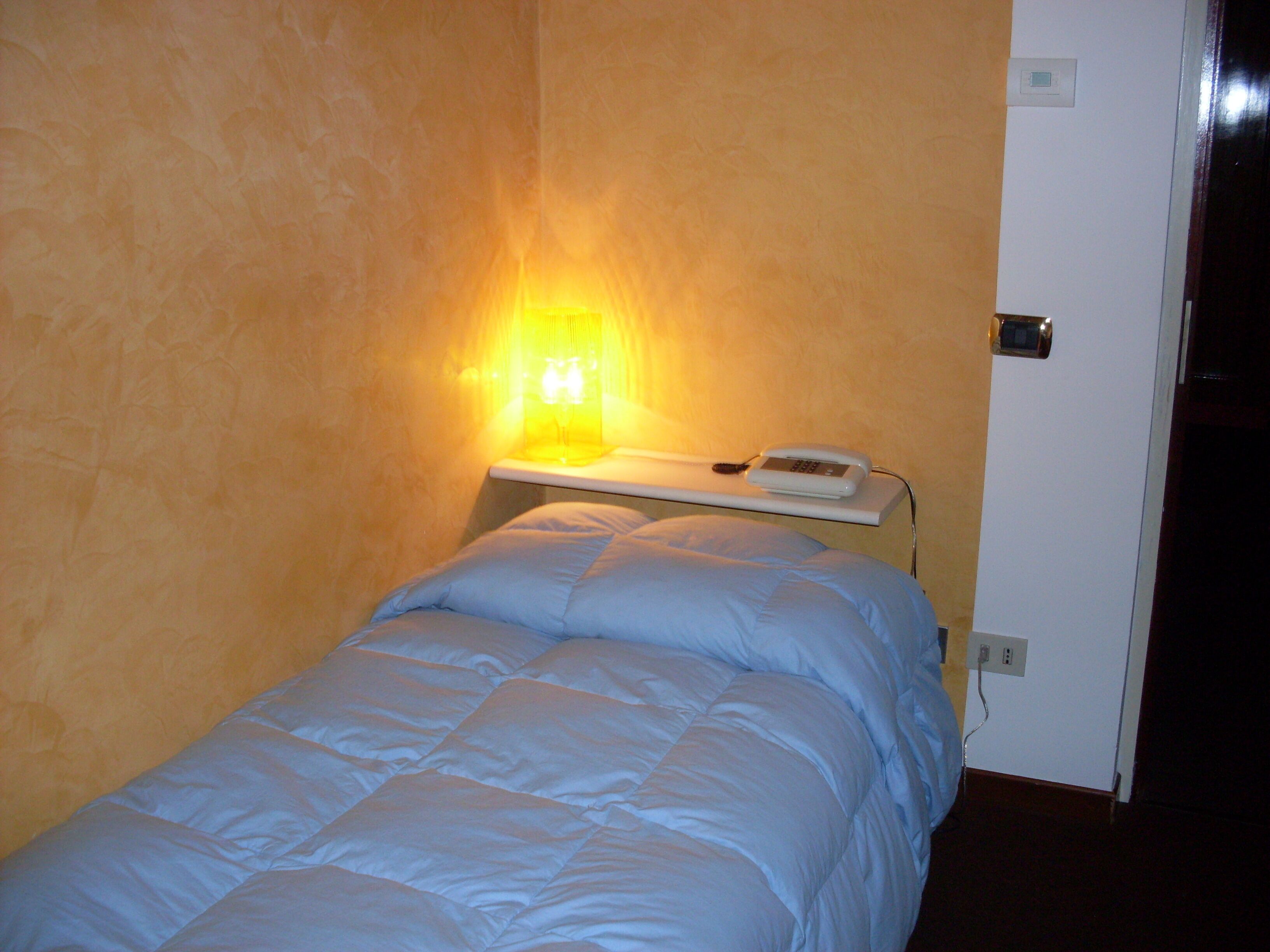 A small, single-bed room with a bedside table, a lamp, and a phone.