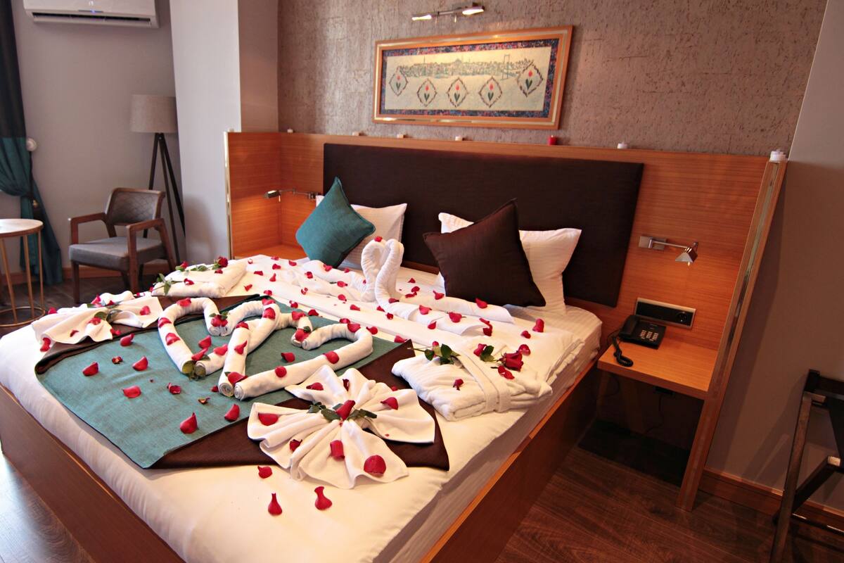 A hotel room with a neatly made bed, a wooden headboard, a bedside table with a phone, and a chair by the window.