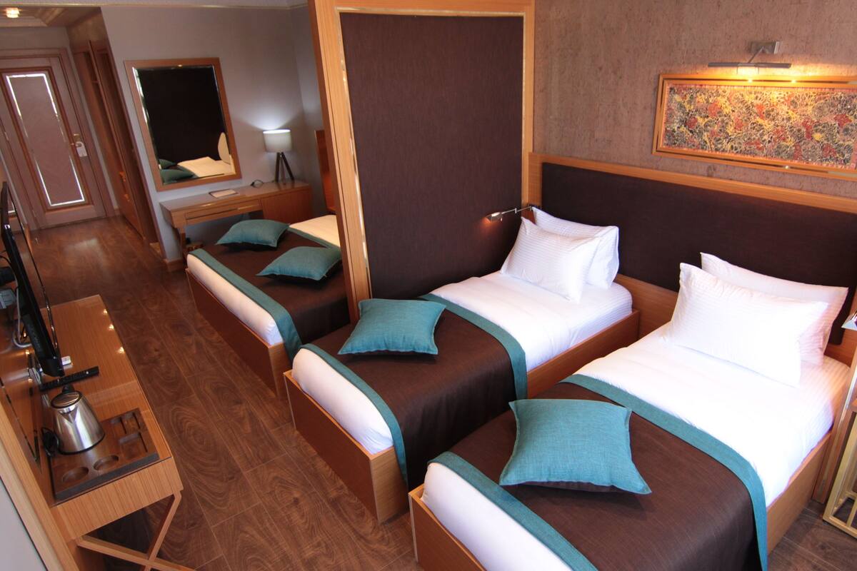 A hotel room with two single beds, a small desk, a mirror, a lamp, and a painting on the wall.