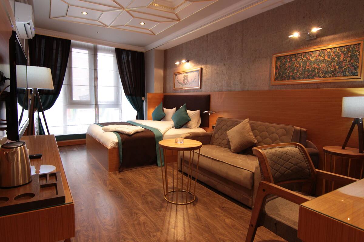 A hotel room with a bed, a sofa, a small table, a desk, and a TV.