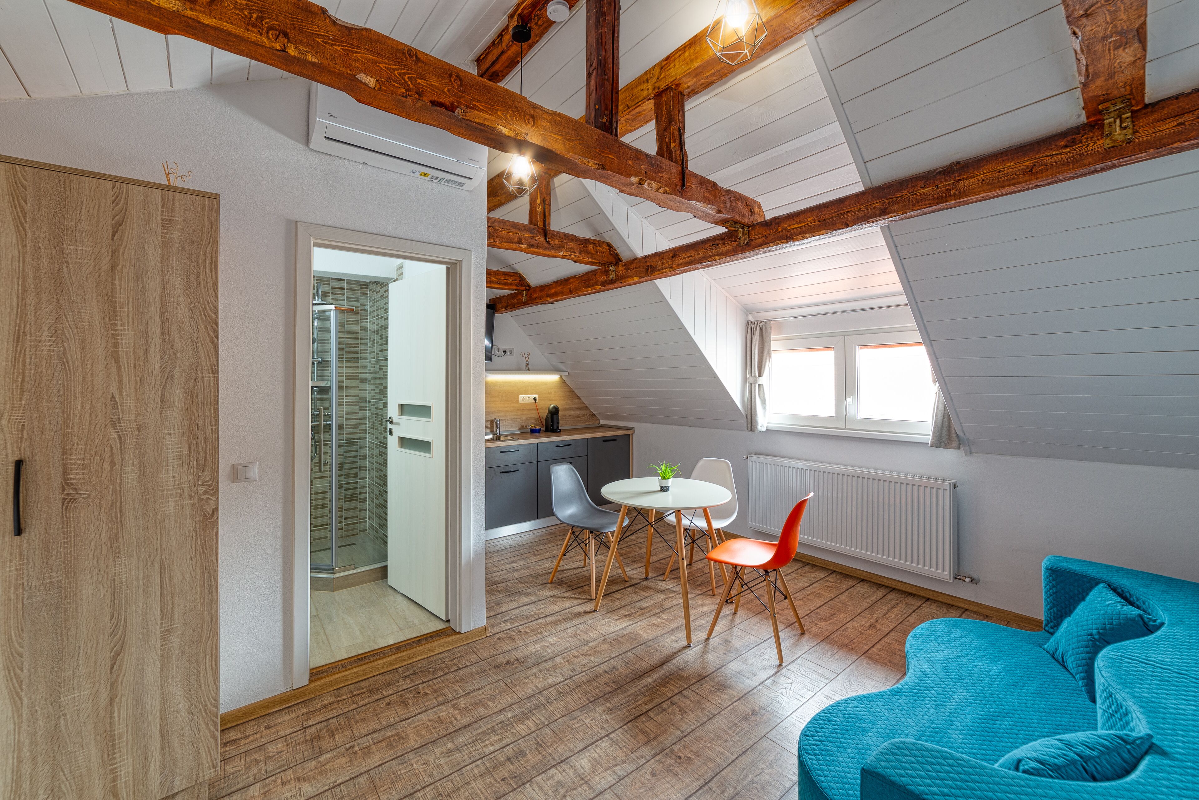 Un loft moderno con vigas de madera a la vista, una zona de comedor con mesa y sillas redondas, y un ventanal luminoso.
