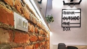 A room with exposed brick walls, a white ceiling, and a black-framed window. There is a sign on the wall that reads "THINK OUTSIDE THE BOX". - T House (Sibiu)