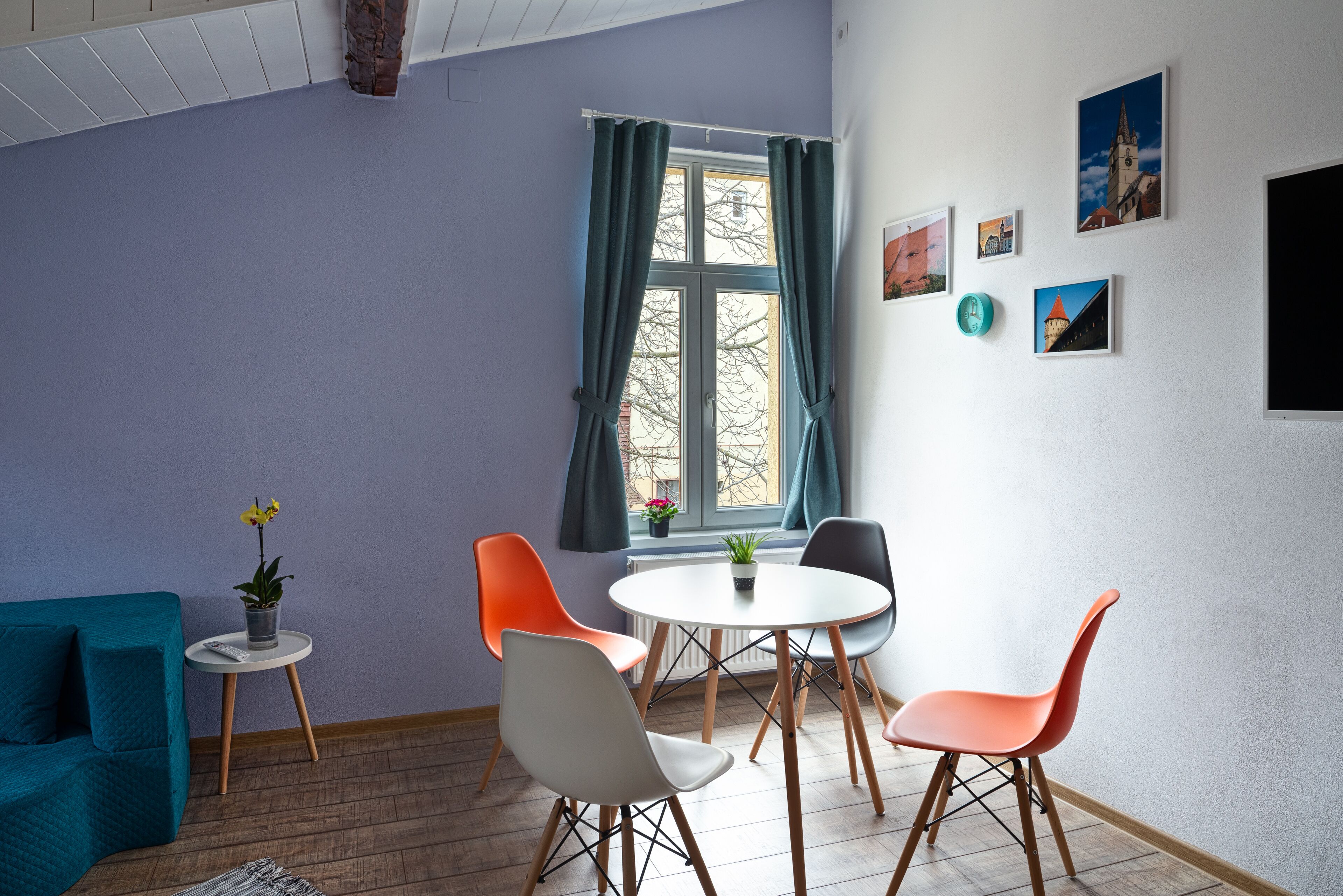 Une pièce avec un canapé de couleur turquoise, une petite table sur laquelle est posée une plante en pot, et une table ronde entourée de quatre chaises.