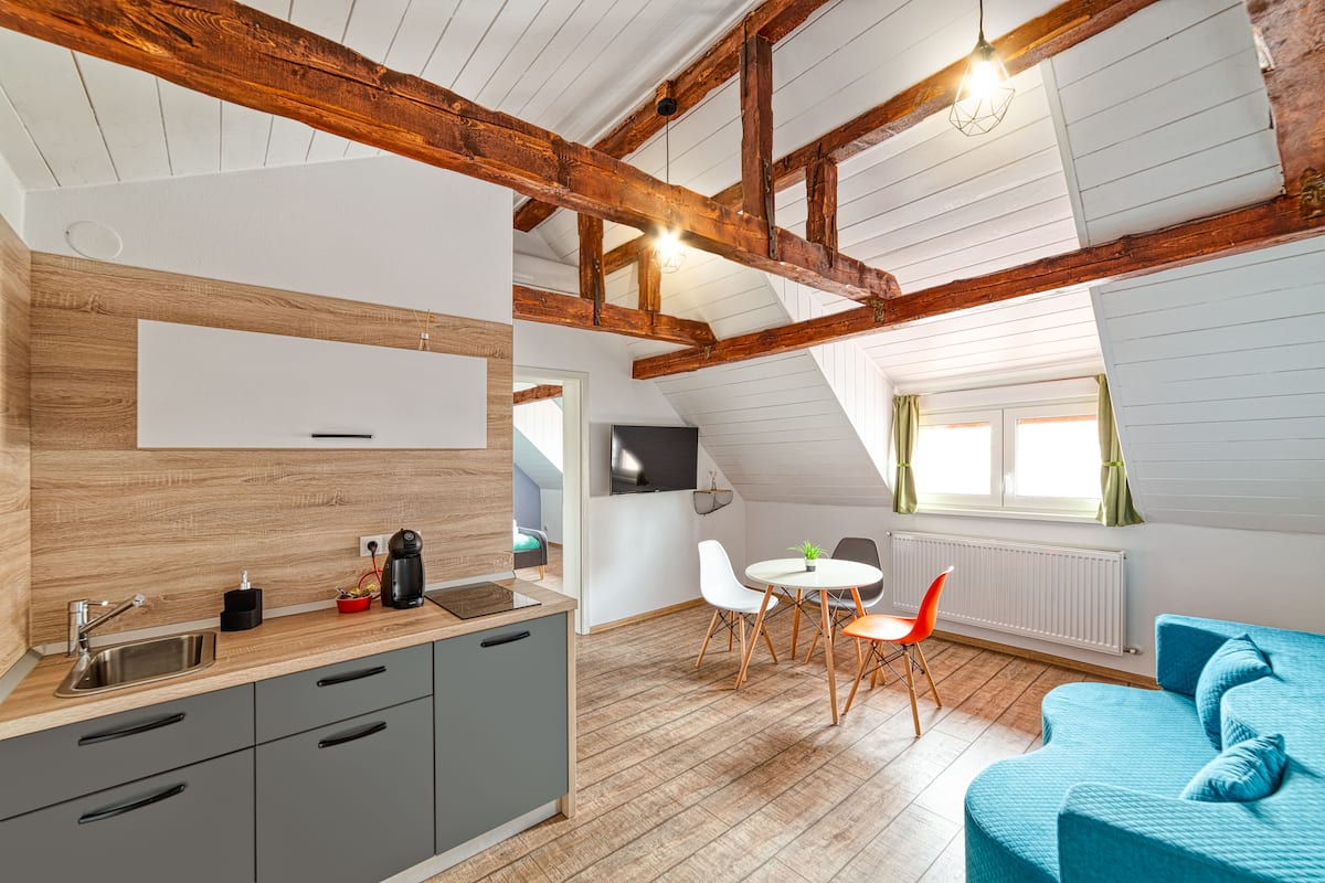 A modern kitchen with a wooden ceiling, a dining area with a round table and chairs, and a blue sofa in a living area.