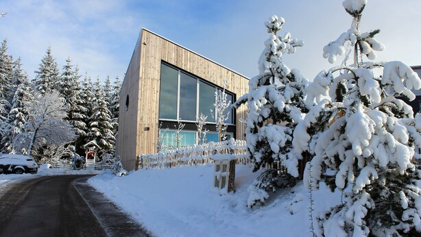 Een modern gebouw met grote ramen, omgeven door met sneeuw bedekte bomen en een heldere lucht.